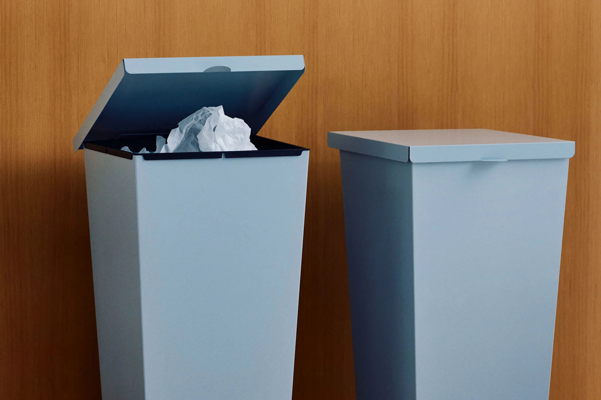 Deux poubelles bleu clair contre un mur en bois, l'une ouverte avec du papier froissé.
