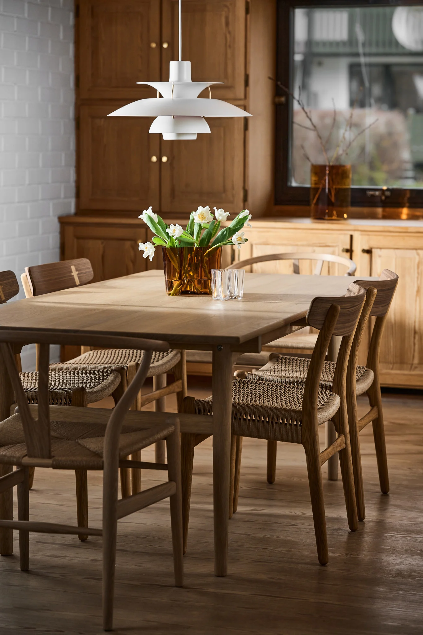 Lampes scandinaves : la suspension blanche PH 5 de Louis Poulsen est suspendue au-dessus d'une table dans une salle à manger scandinave.