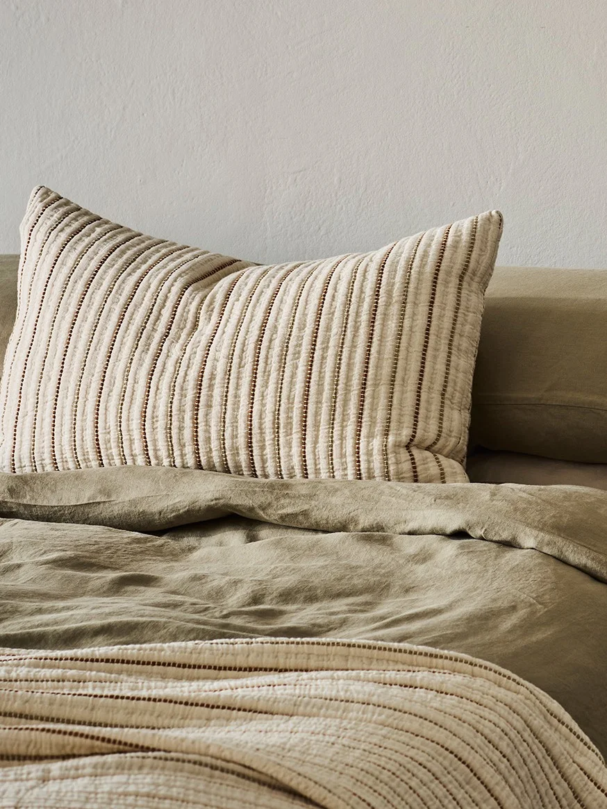 Un oreiller rayé sur un lit vert olive avec une couverture rayée assortie.