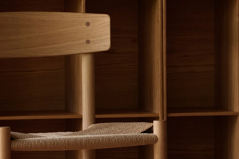 Une chaise en bois clair avec une assise tressée devant une étagère murale en bois à casiers carrés et un parquet à motifs.