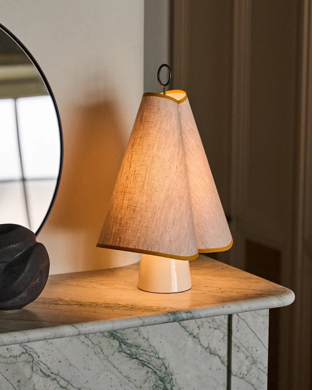 Une lampe de table unique avec un abat-jour double conique en tissu bordé de jaune, diffusant une lumière chaude sur un plateau en marbre vert.