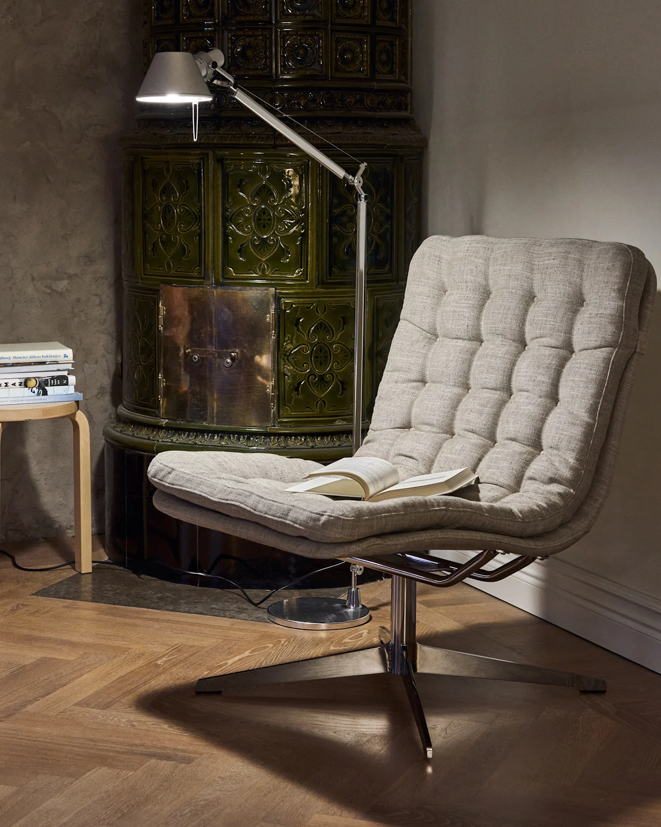 Coin lecture douillet avec un fauteuil capitonné, une lampe de lecture réglable et un poêle en faïence vert foncé.