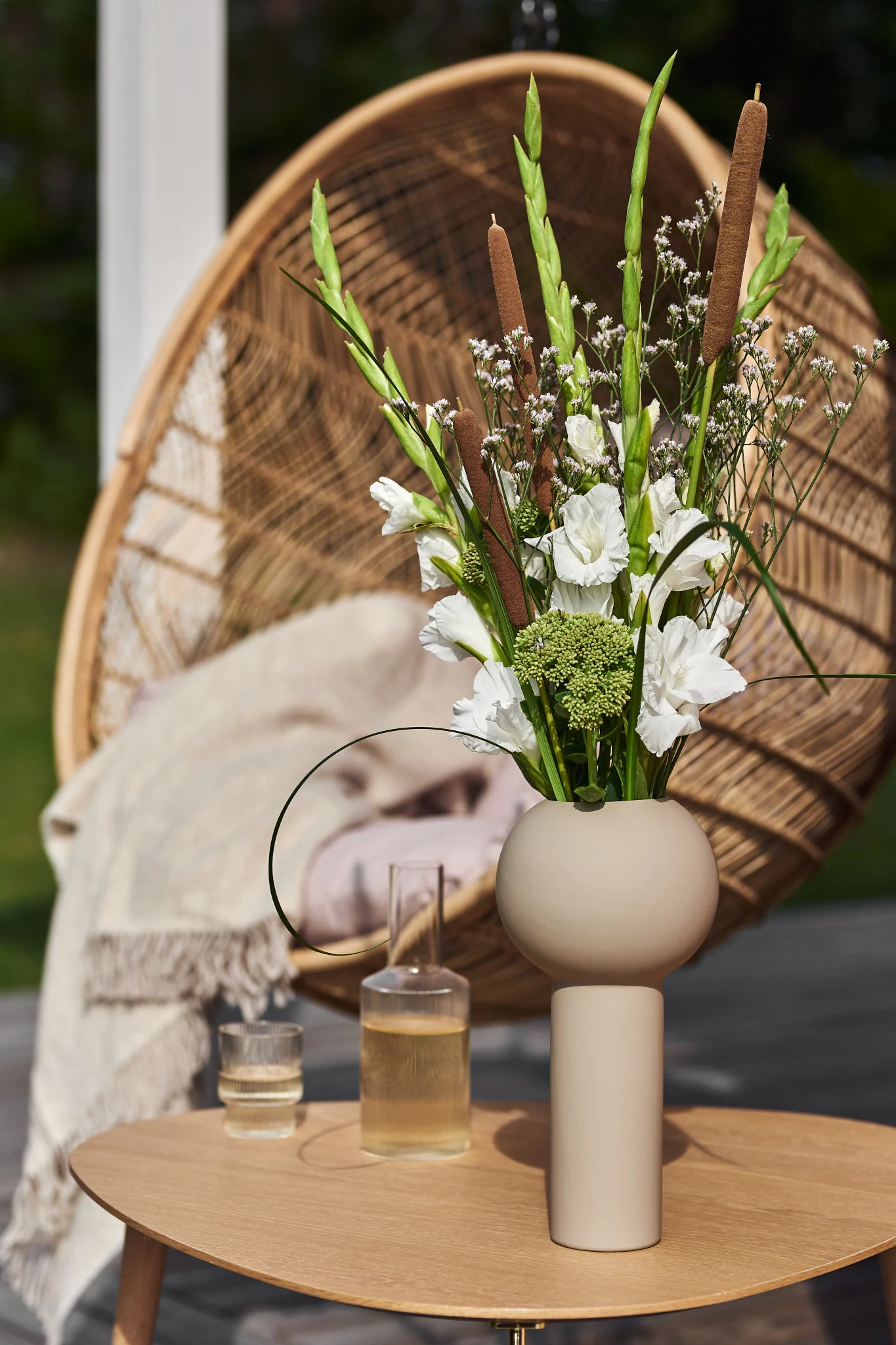 Sur une table dans un jardin se trouve le grand vase Pillar beige de Cooee Design, rempli de fleurs printanières fraîchement coupées.