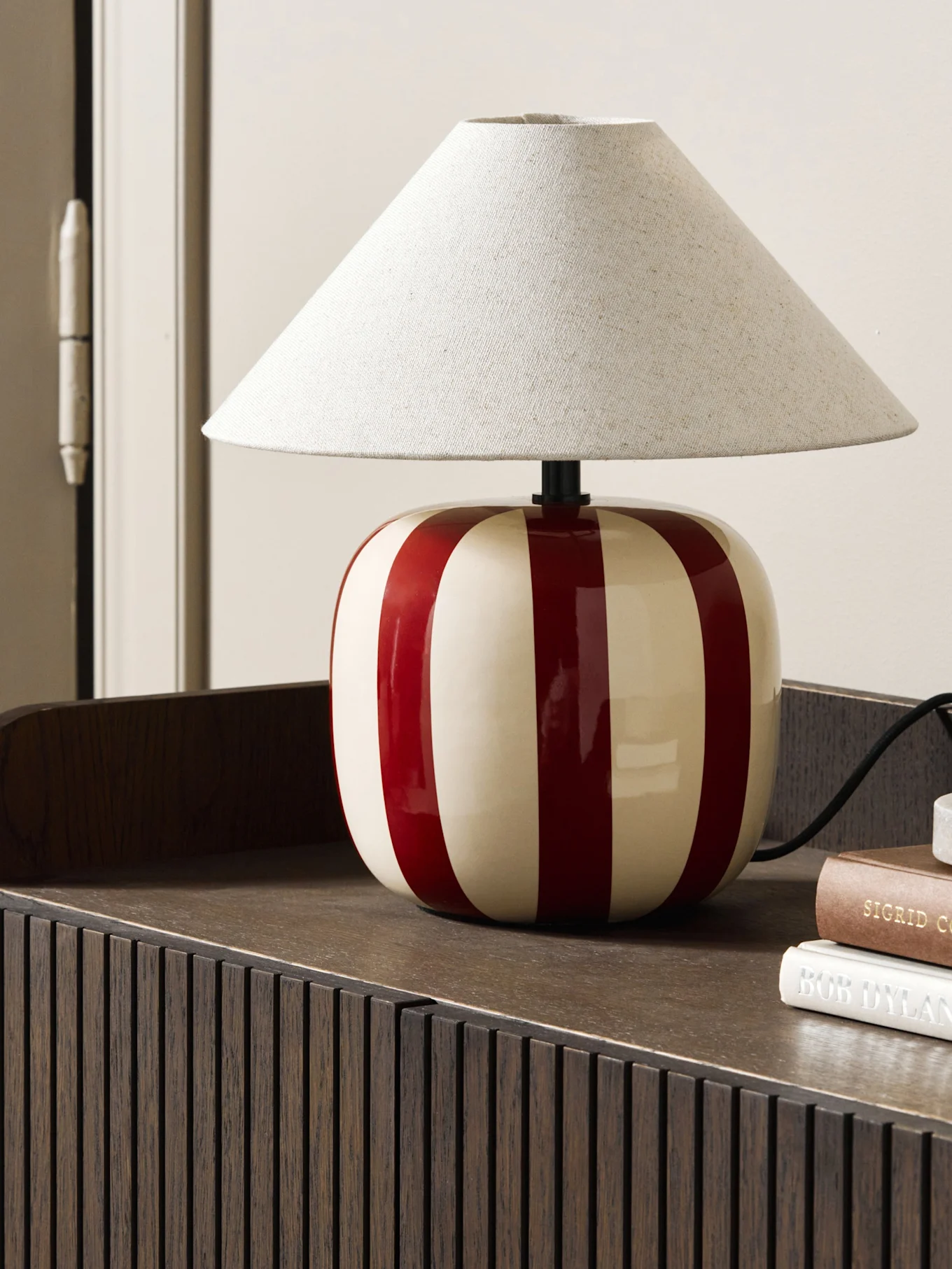Lampe de table bleu clair en forme de champignon sur un livre brun-rouge, sur une étagère festonnée.