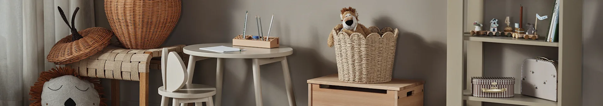 Chambre d'enfant avec un jouet en peluche lion dans un panier tressé, une petite table en bois avec des crayons et une étagère avec des jouets et des livres.