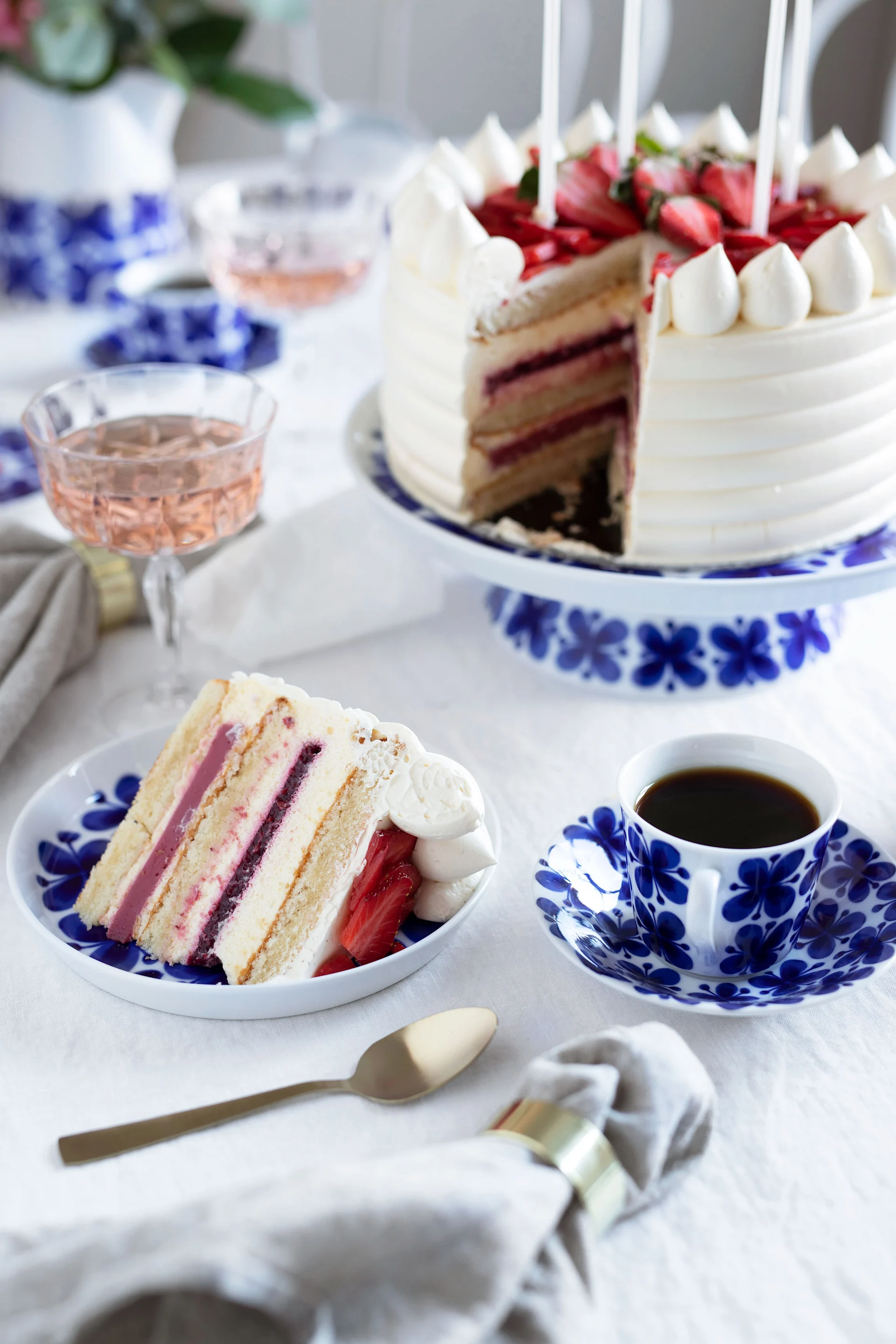 Gâteau aux fraises avec une part coupée, servi sur de la vaisselle à motifs bleus et blancs avec du café et du rosé.