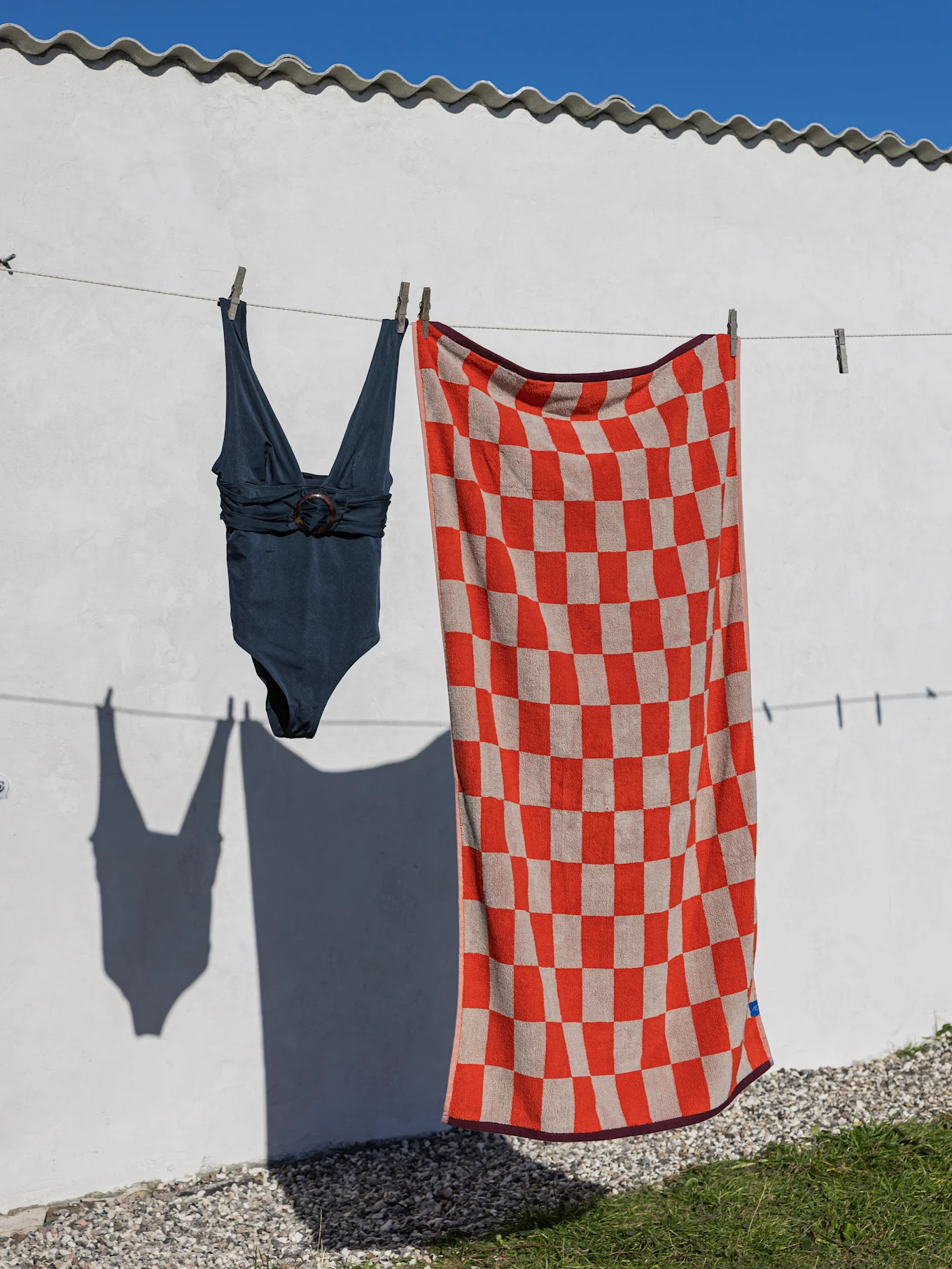 Un maillot de bain une pièce bleu foncé et une serviette de plage à carreaux rouges et beiges accrochés à une corde à linge.