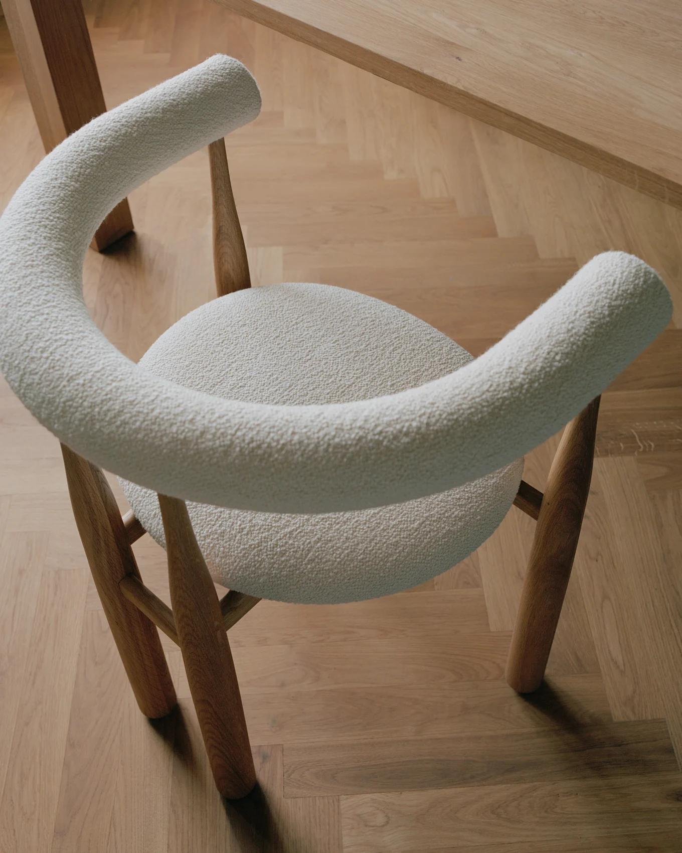 Chaise moderne avec un revêtement en bouclé crème clair et des pieds en bois, sur un parquet en bois clair.