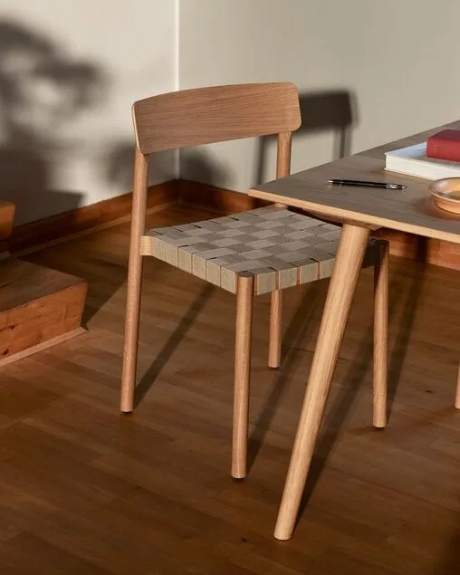 Une chaise en bois clair avec un siège tissé à carreaux à côté d'une table avec des livres et un stylo.
