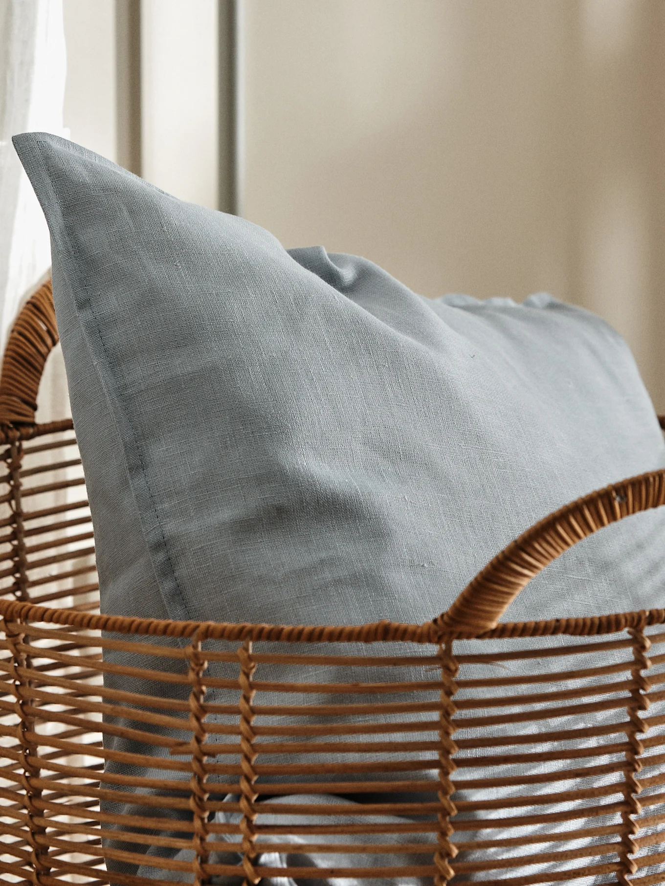 Coussin texturé bleu clair niché dans un panier en osier marron.