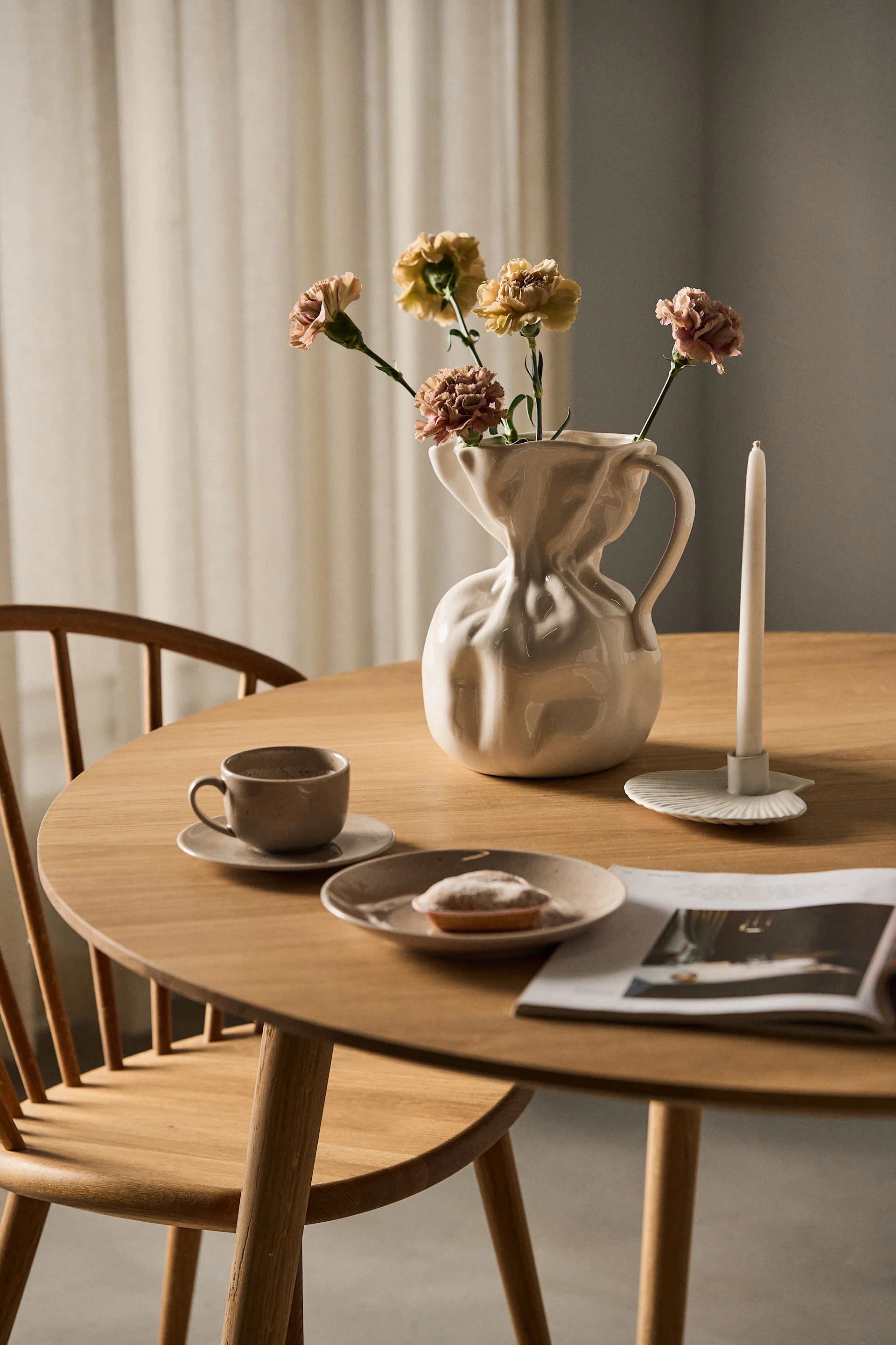Sur une table à manger se trouve le vase blanc Crumple de Byon avec quelques fleurs coupées.