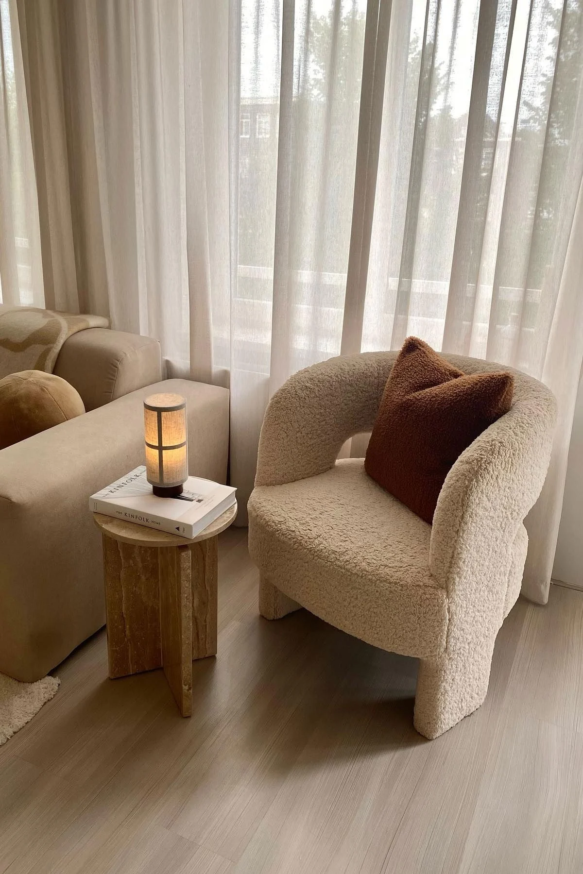 Sur une table basse en marbre repose un livre, sur lequel est posée la lampe de table Hashira d'Audo Copenhagen, à gauche un canapé, à droite un fauteuil.