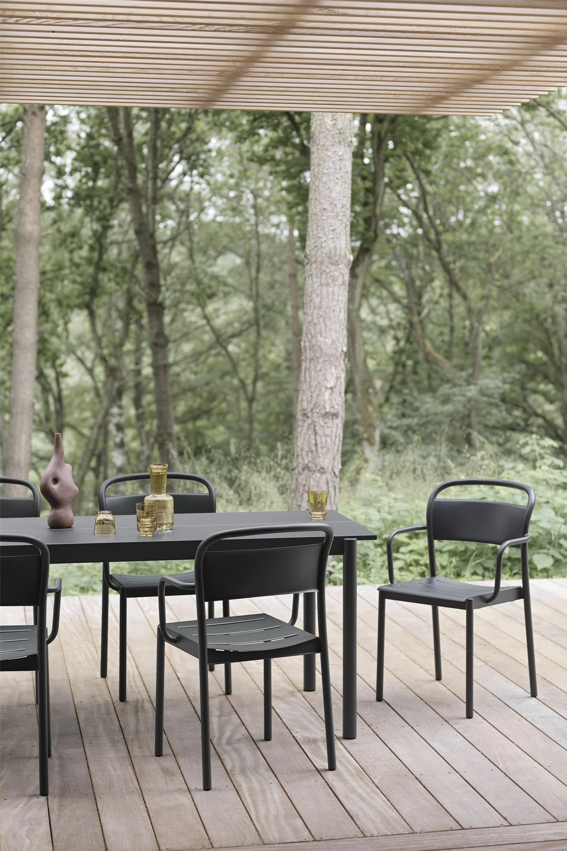 Une terrasse couverte en bois avec une table et des chaises noires de la collection Linear de Muuto.