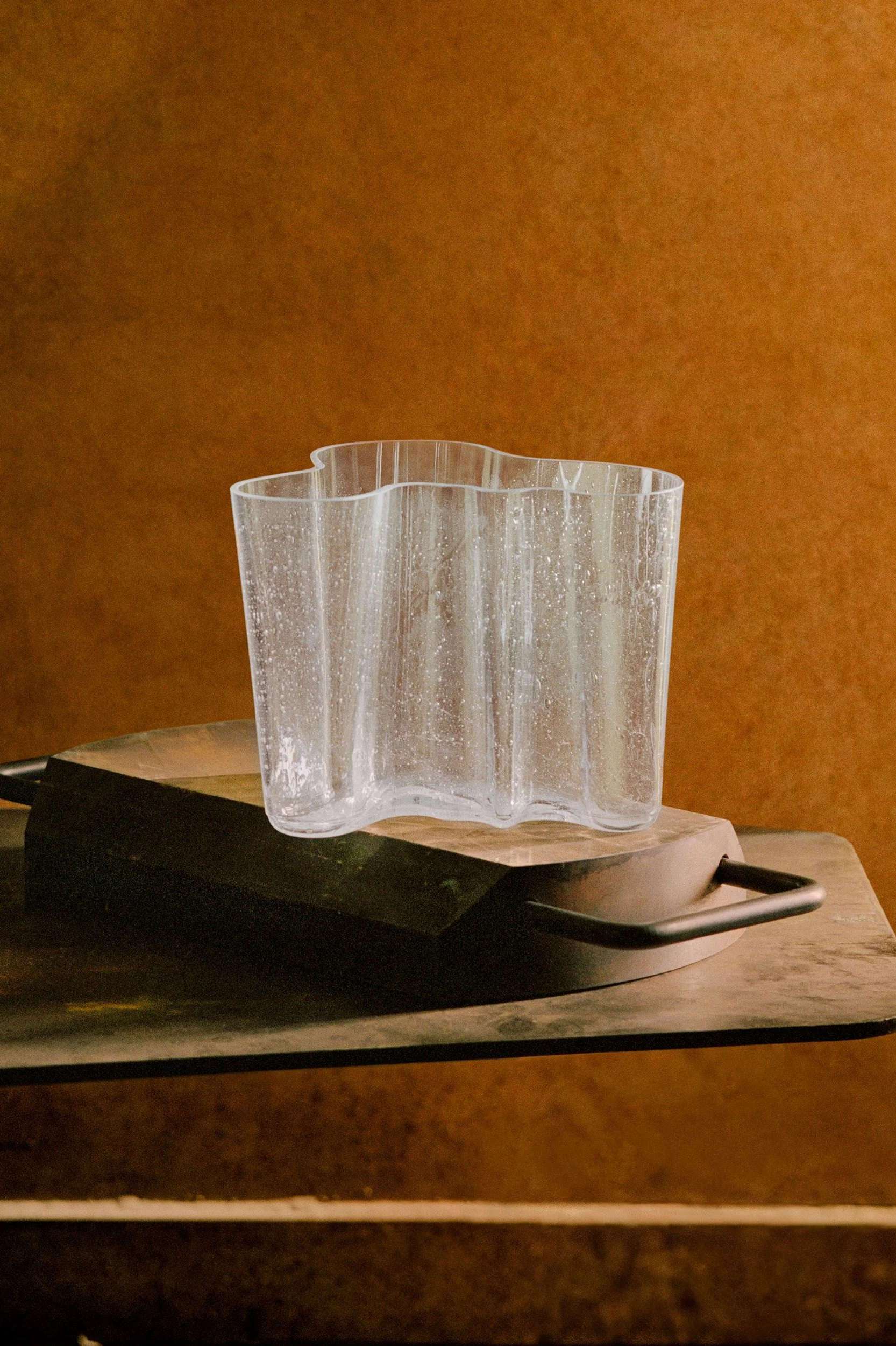Vase en verre ondulé transparent à la surface texturée, posé sur une planche en bois.