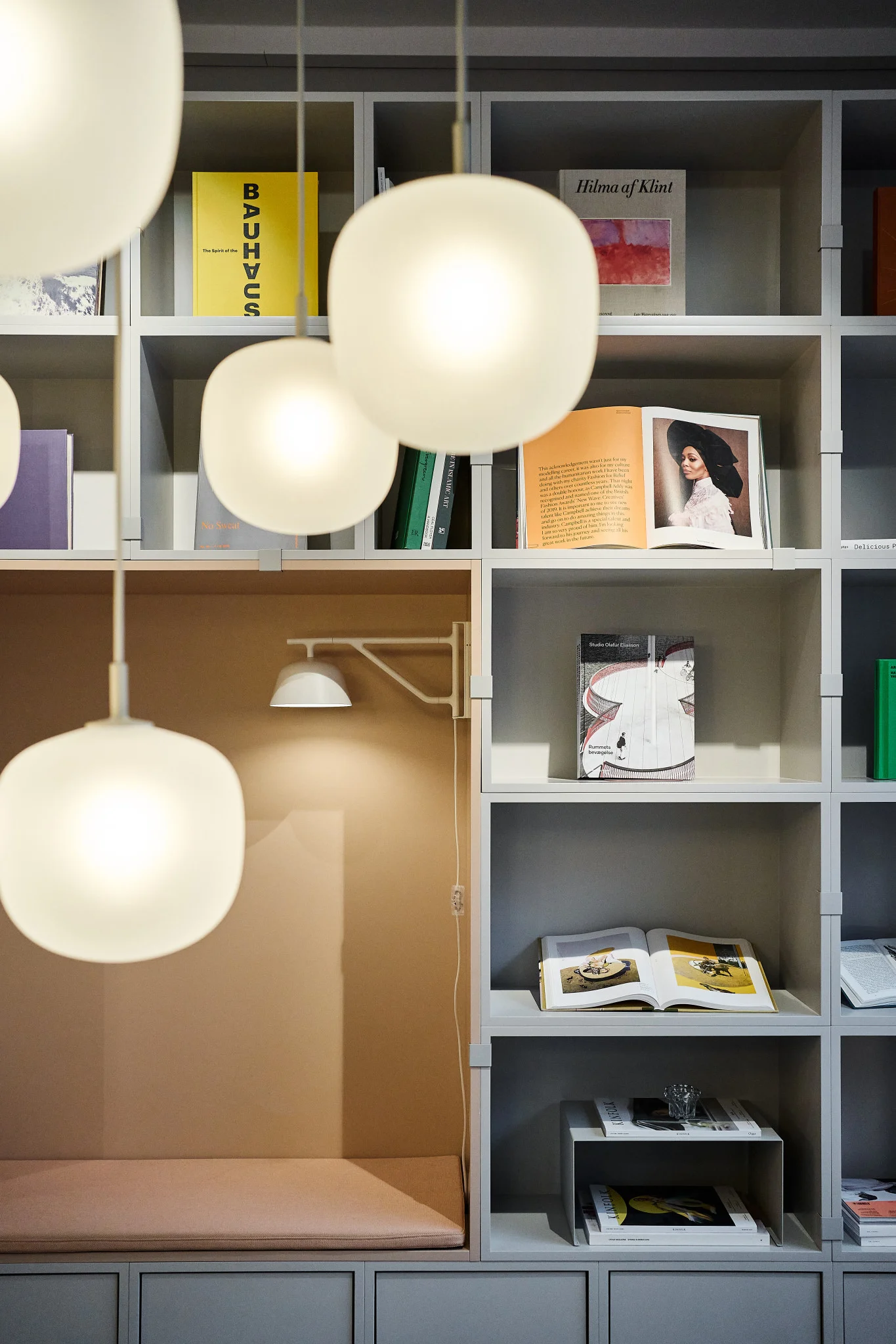 Une étagère bien rangée, décorée de livres, avec plusieurs lampes suspendues Rime de Muuto au premier plan.
