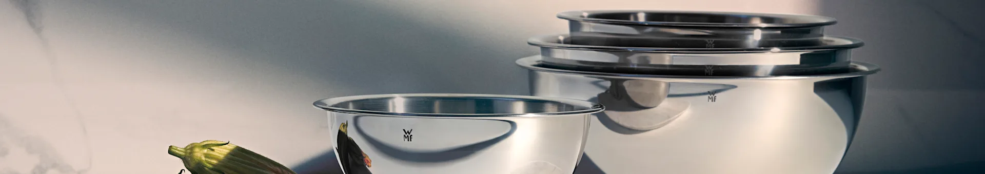 Saladiers mélangeurs brillants WMF en acier inoxydable, un devant, les autres empilés, avec un légume vert.
