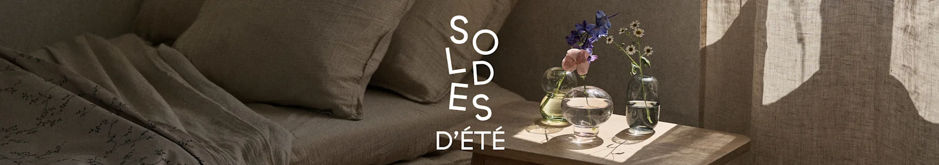 Bannière Soldes d'Été avec un lit en linge de lit beige et une table de chevet en bois avec des fleurs dans des vases en verre.