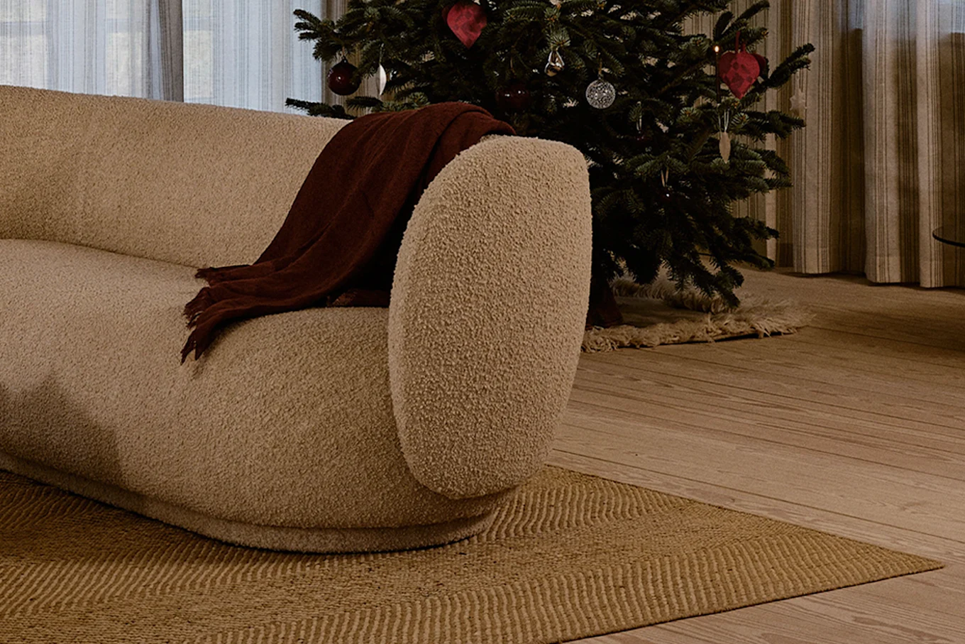 Canapé incurvé crème avec plaid marron, à côté d'un sapin de Noël décoré dans un salon douillet.