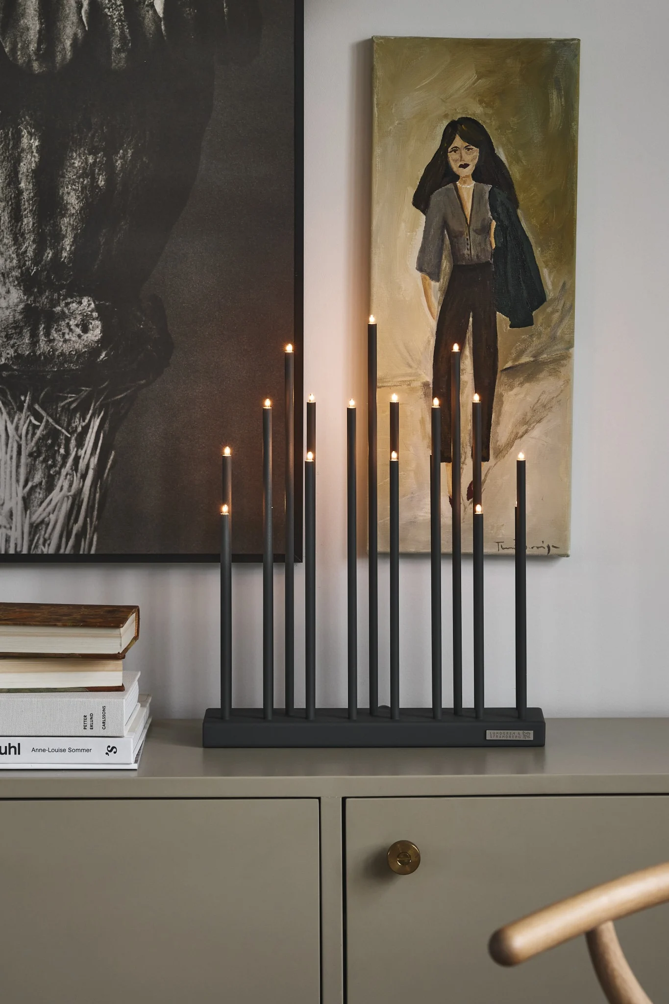 Le bougeoir de l'Avent Elflugan est posé sur une commode et brille avec des tableaux rustiques en arrière-plan. 