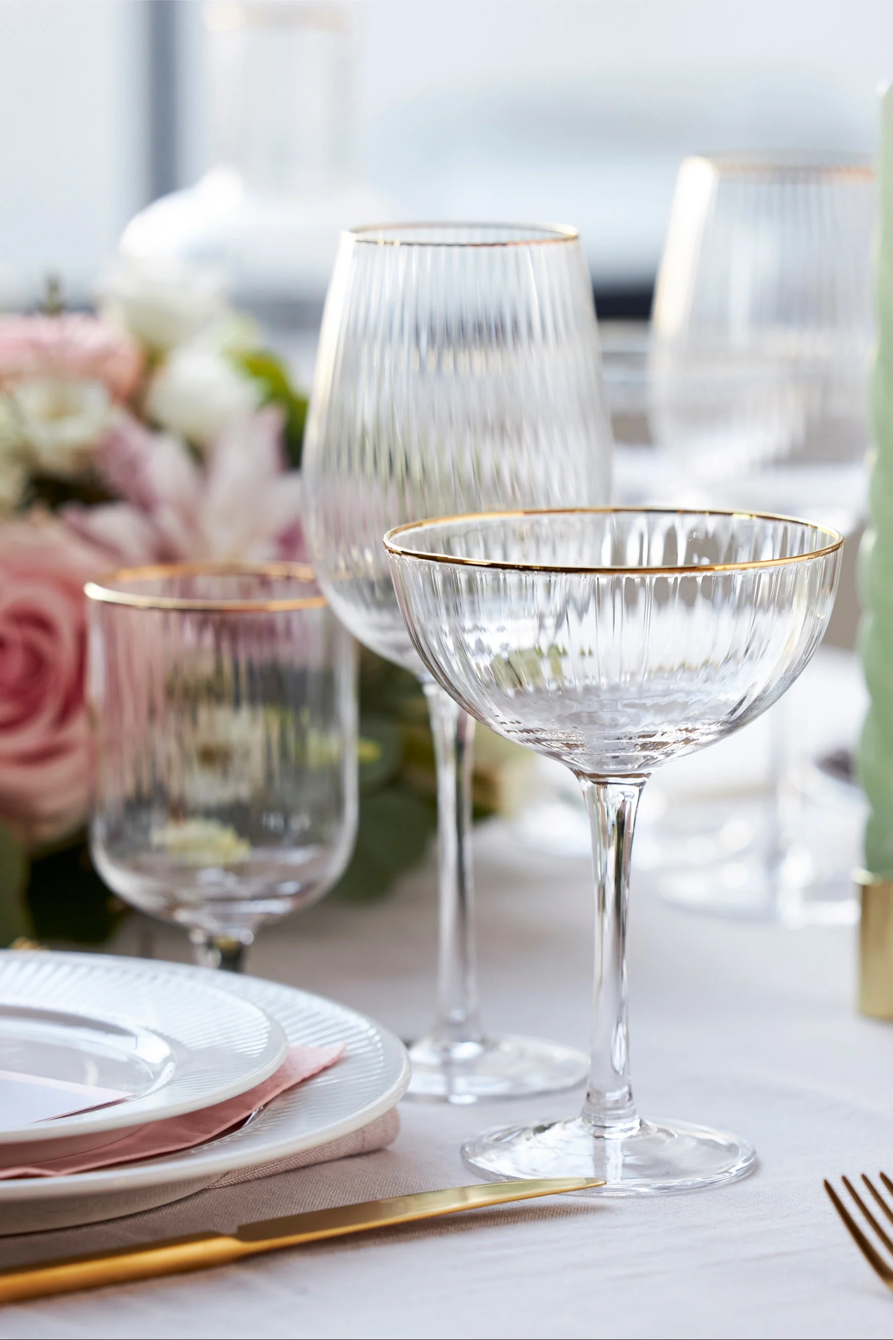 Les verres de la collection Palermo de Lyngby Glas ont un élégant bord doré et sont présentés ici sur une table élégamment dressée en blanc, rose et or.
