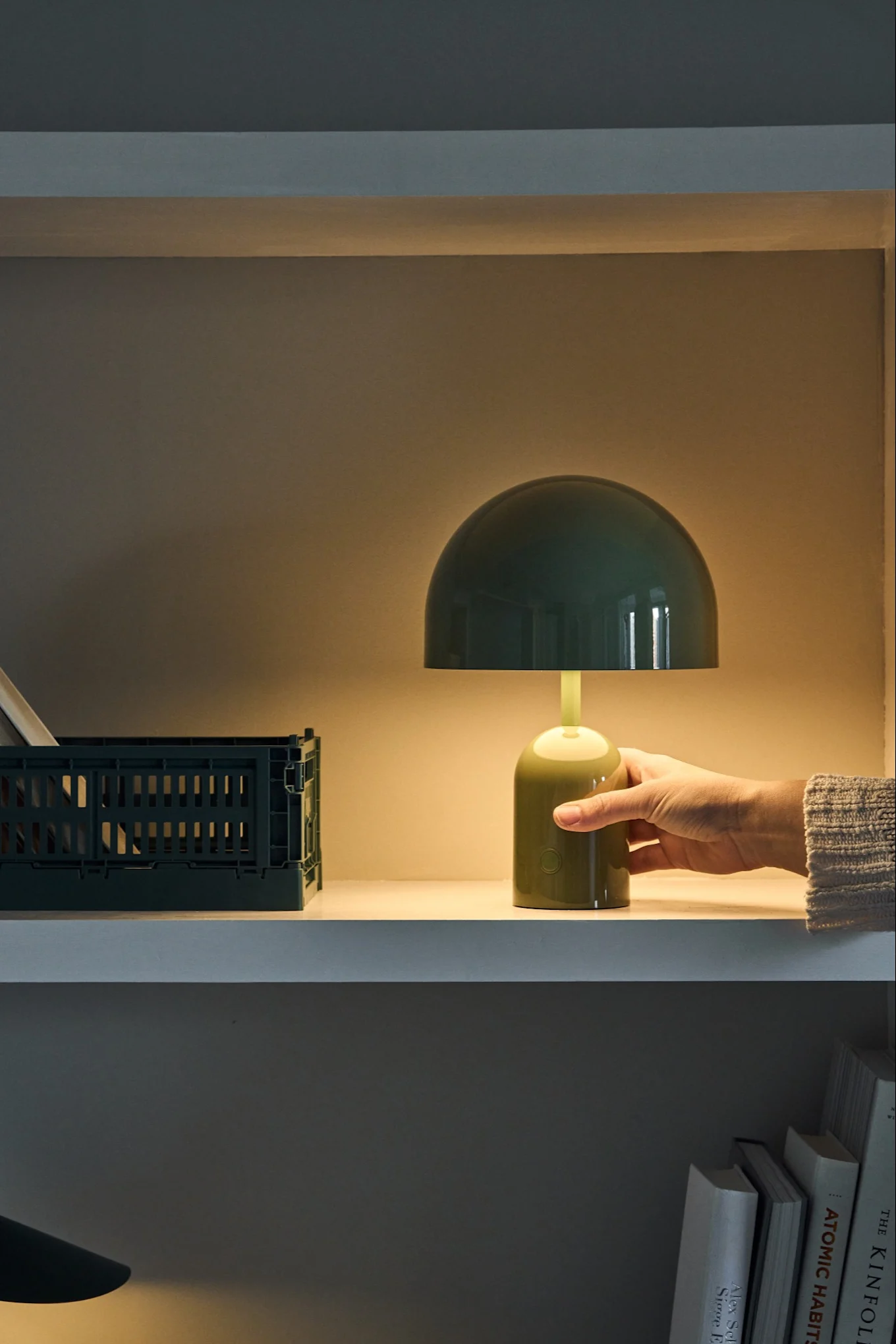 La lampe portable verte Bell de Tom Dixon s'allume d'un simple geste de la main sur une étagère. 