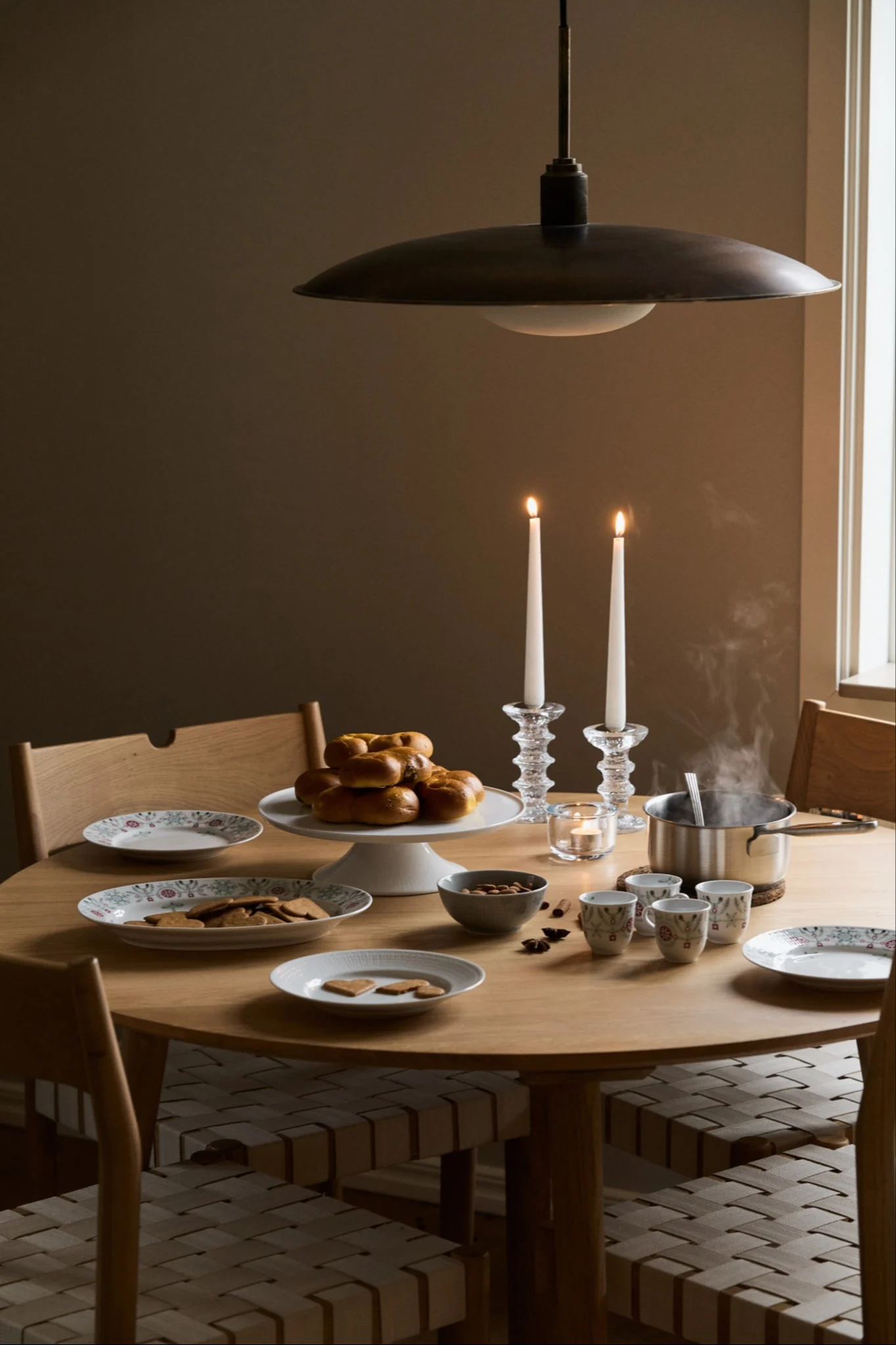 Une table de Noël dressée avec la vaisselle de la collection Swedish Grace Winter de Rörstrand, accompagnée de bougies et de pâtisseries.