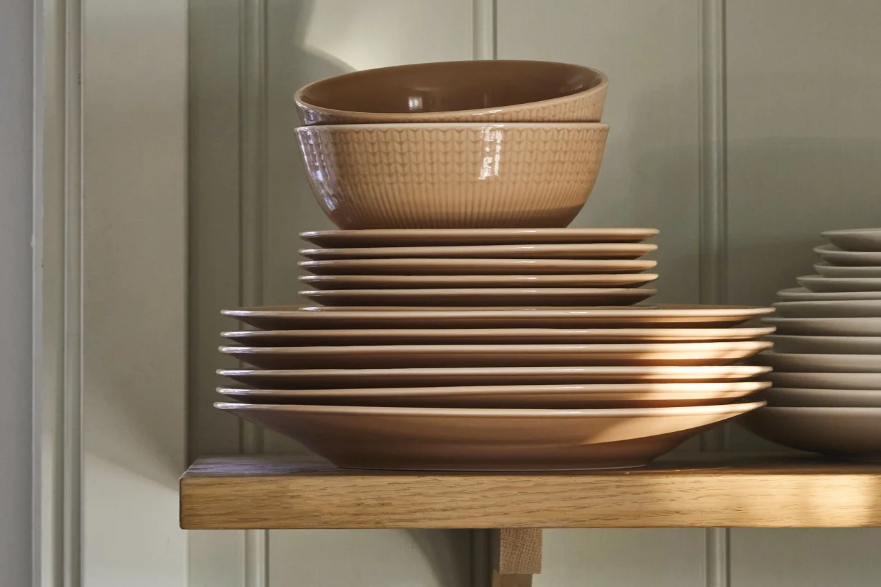Piles d'assiettes et de bols en céramique marron clair et texturés sur une étagère en bois.
