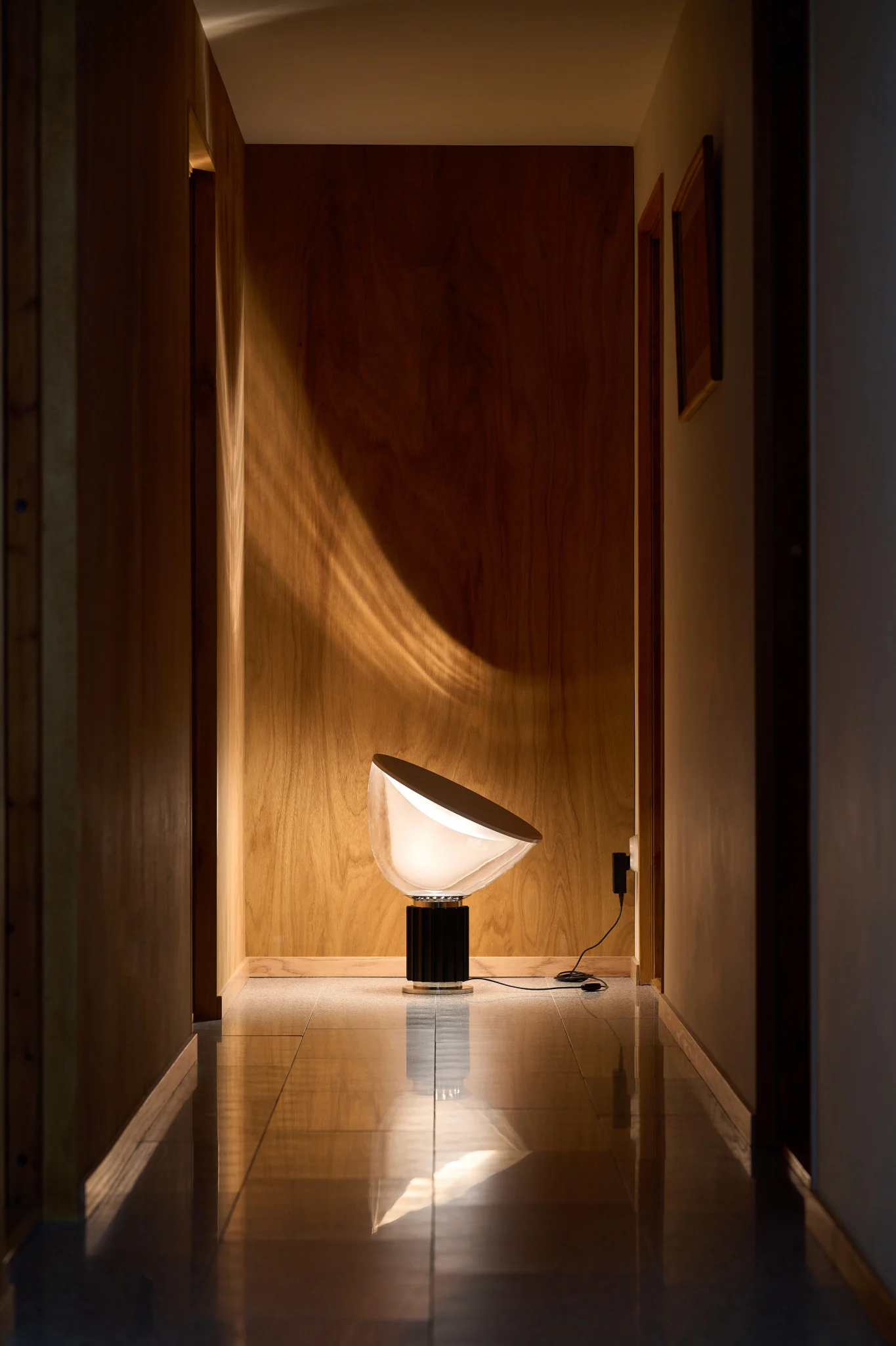 Cuisine moderne avec un îlot sombre, des tabourets de bar noirs et trois suspensions noires. La table est dressée avec de la vaisselle, et de grandes fenêtres encadrent l'arrière-plan lumineux.