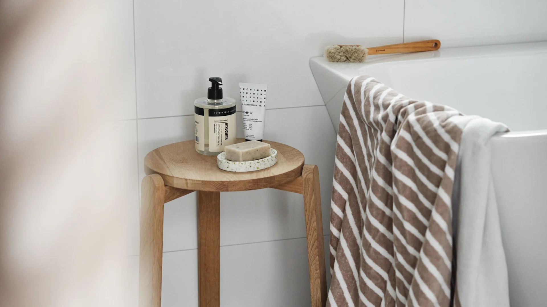 Cadeau pour la Saint-Valentin : offrez une journée spa et les accessoires nécessaires. Ici, la serviette de bain Stripes de NJRD est suspendue au-dessus d'une baignoire, à côté d'un tabouret sur lequel sont posés un savon et un porte-savon Humdakin.