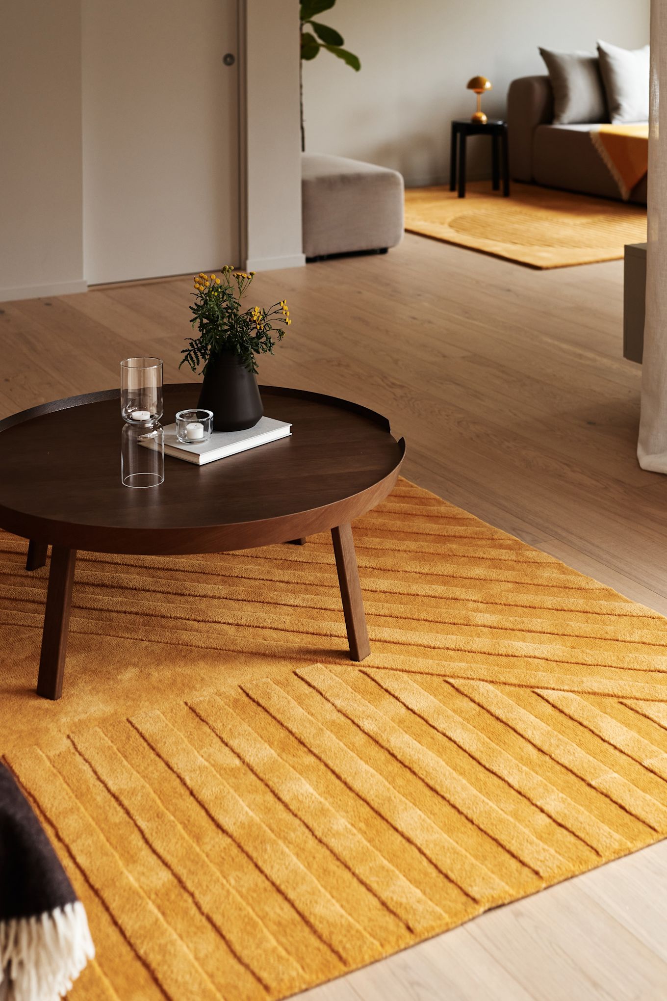 Tapis pour le salon : Le tapis en laine jaune Levels stripes in Jaune de NJRD se trouve dans un salon harmonieux avec une table d'appoint en bois brun foncé.