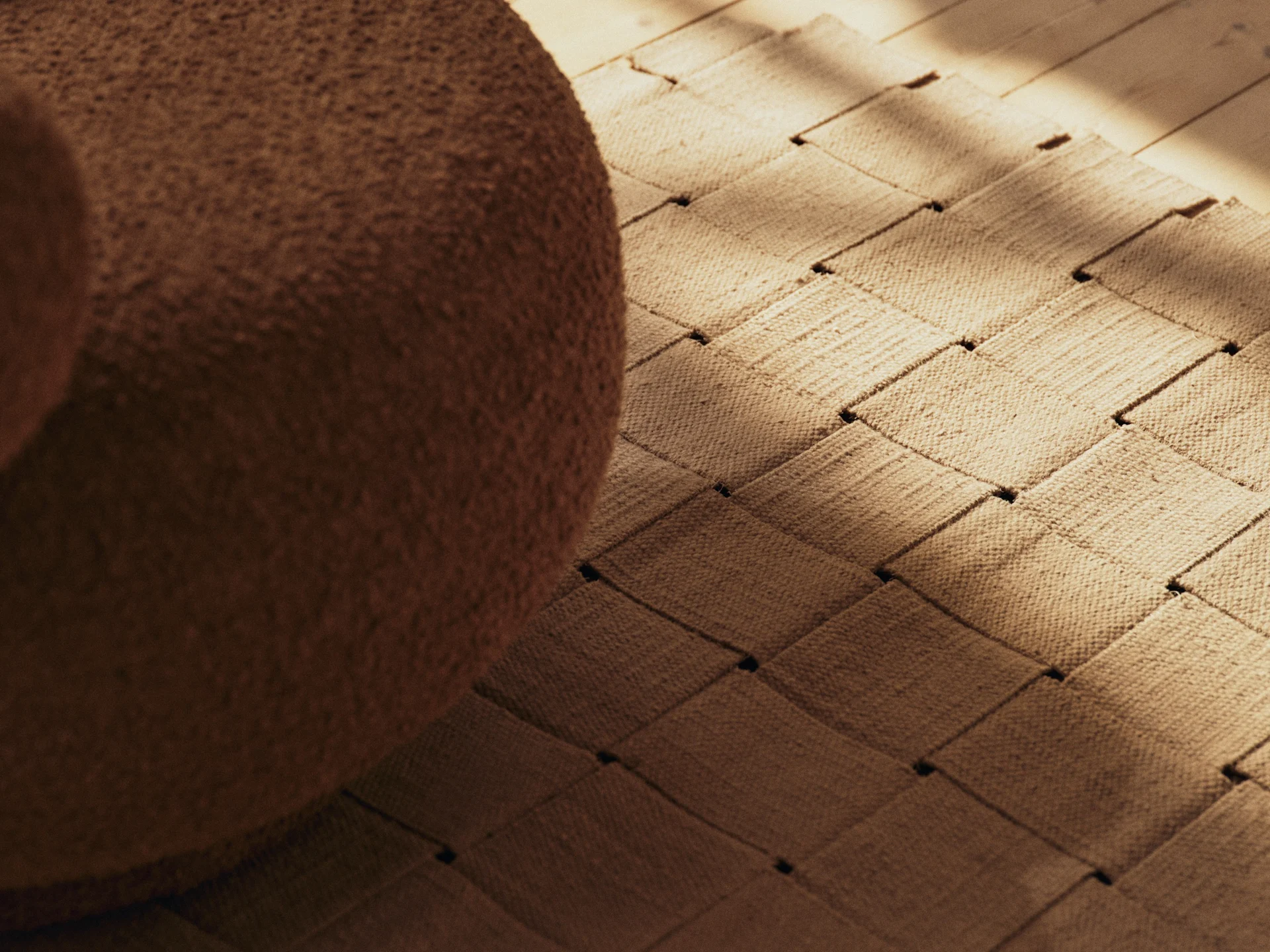 Meuble bouclé marron, un tapis tissé et un parquet en bois avec des ombres ensoleillées.