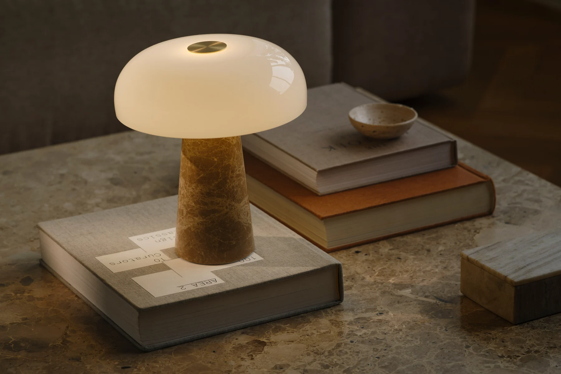 Une lampe de table en forme de champignon avec abat-jour en verre blanc et base conique en marbre, sur une table en marbre avec des livres empilés.