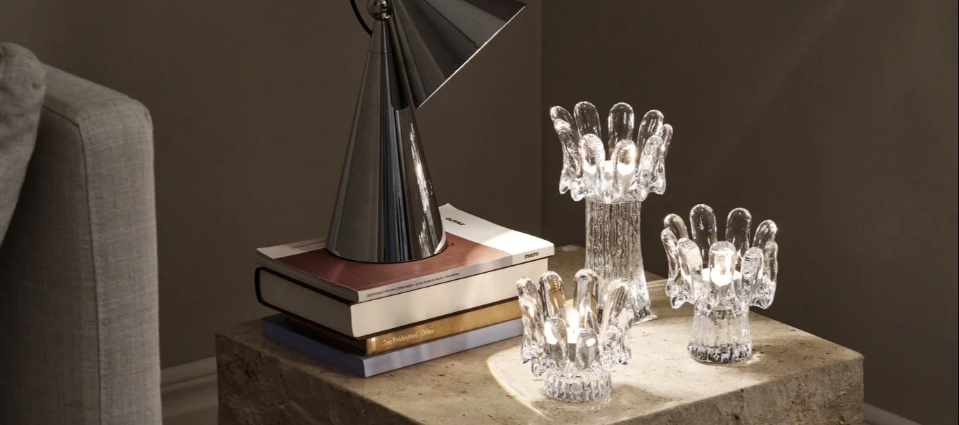 Tendances déco 2026 : sur une table d'appoint en marbre trône une lampe de table Tom Dixon qui éclaire trois bougeoirs en verre issus de la collection Solros de Kosta Boda.