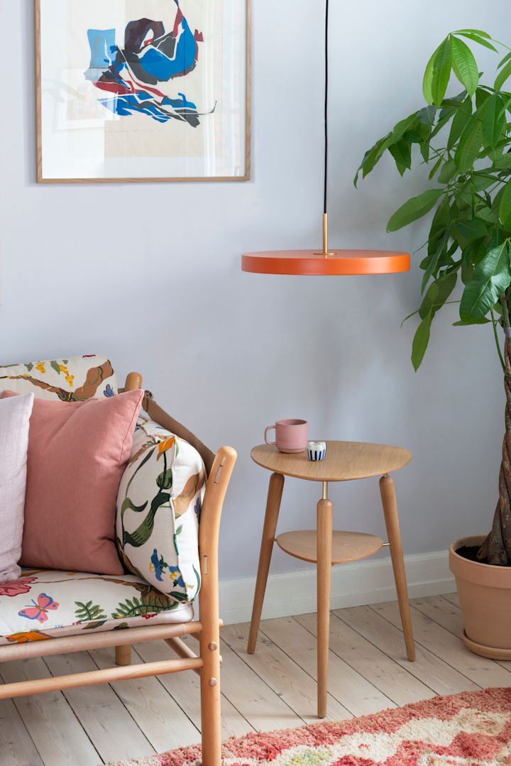 Les tons orange conviennent parfaitement au style bohème. Vous voyez ici un banc avec des coussins colorés, à côté duquel se trouvent la table d'appoint My Spot et la suspension Asteria, toutes deux de la marque Umage.