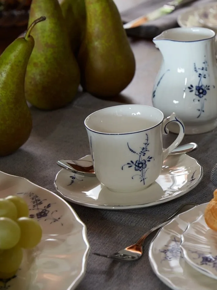 Tasse, soucoupe et pichet en porcelaine blanche avec motif floral bleu sur une table avec poires et raisins.