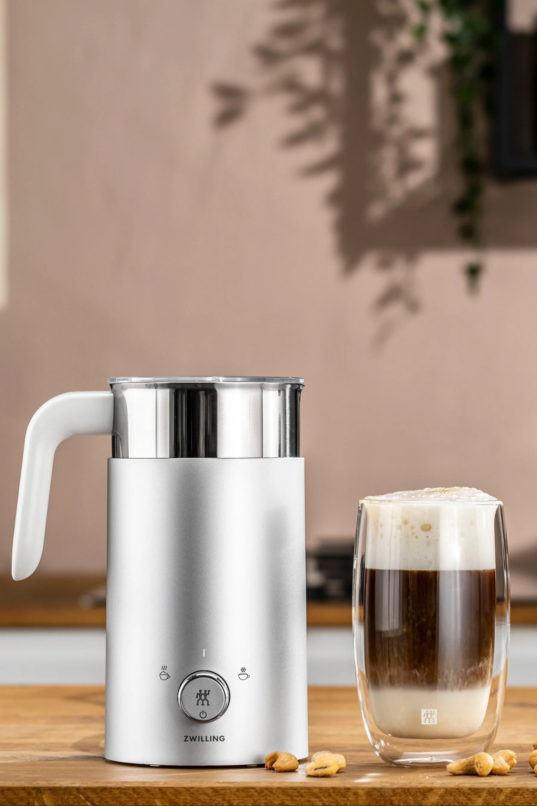 Un mousseur à lait électrique est le cadeau parfait pour les pères qui apprécient un bon cappucchino, car il facilite énormément le travail. Vous voyez ici l'émulsionneur à lait de Zwilling à côté d'une tasse de cappucchino.
