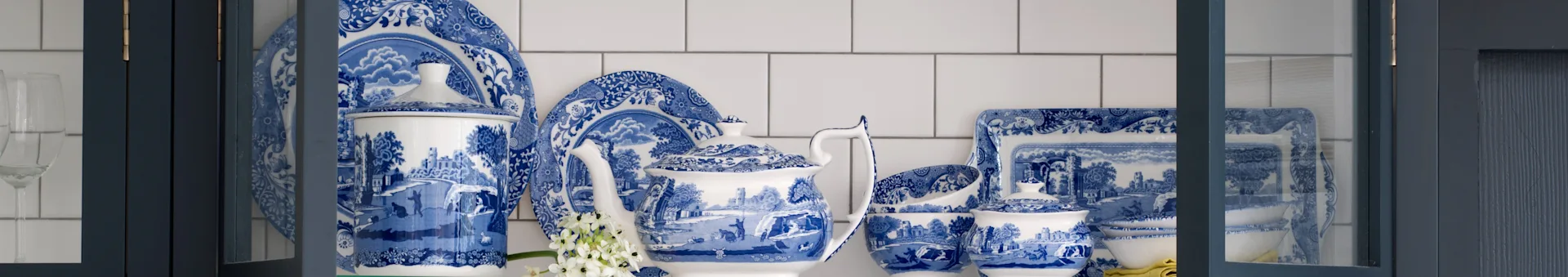 Service de vaisselle en porcelaine bleue et blanche à motifs, avec théière, assiettes et bols dans une armoire bleu foncé.