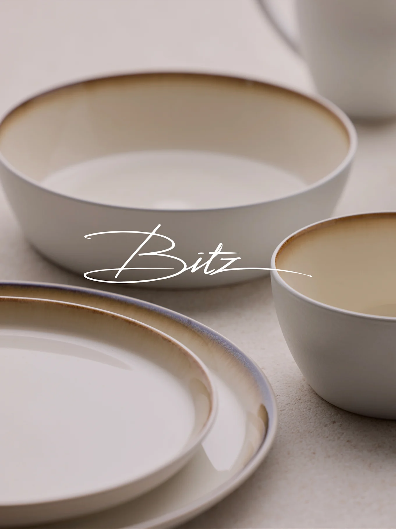 Vaisselle Bitz avec assiettes et bols blanc crème, aux bords dégradés marron et bleu.