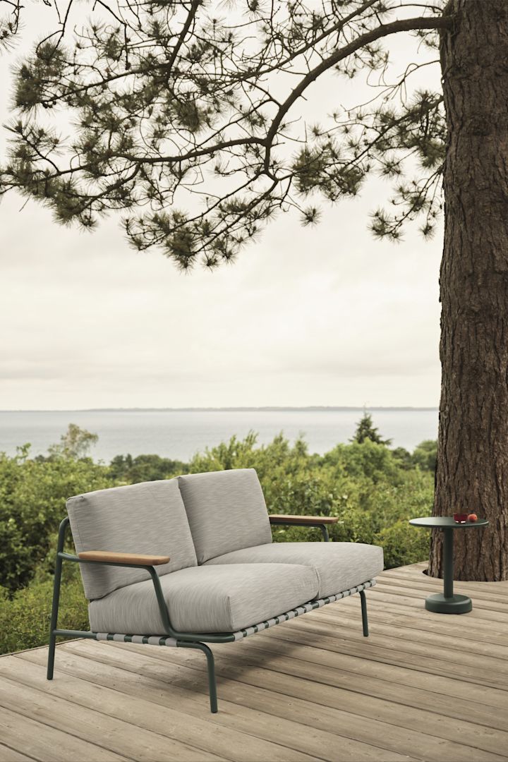 Le canapé d'extérieur Settle de Muuto, ici sur une terrasse avec vue sur l'eau, offre de la place et, grâce à ses coussins épais, un grand confort - un must parmi les tendances de meubles de jardin 2025.
