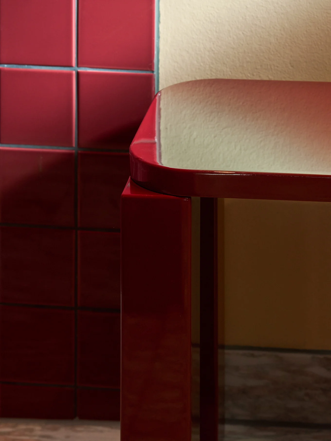 Élégant tabouret rectangulaire rouge brillant aux bords arrondis sur un sol en marbre, à côté d'un mur de carreaux rouges.