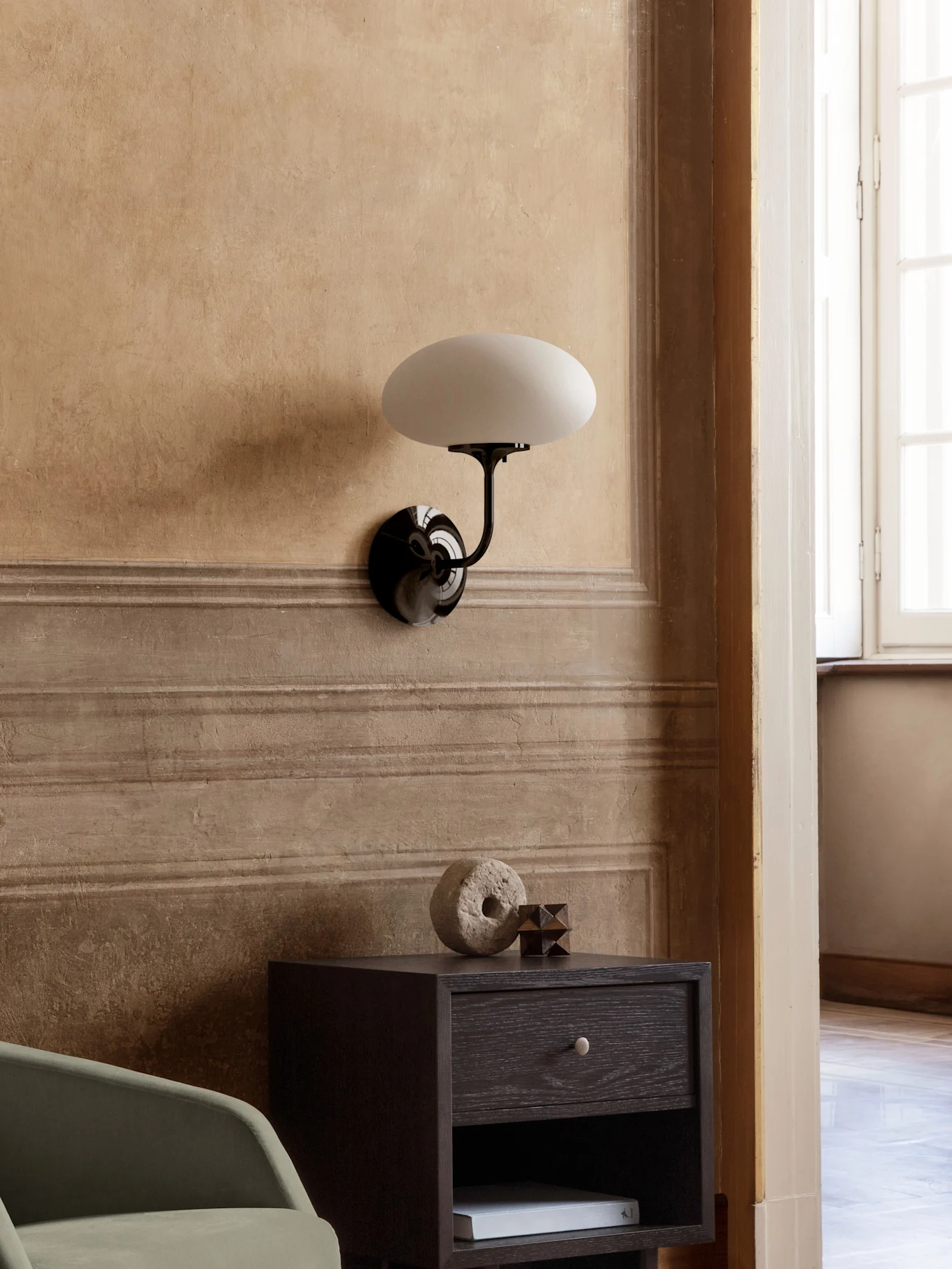 Applique murale noire avec abat-jour ovale blanc, sur table de chevet en bois foncé avec décorations.