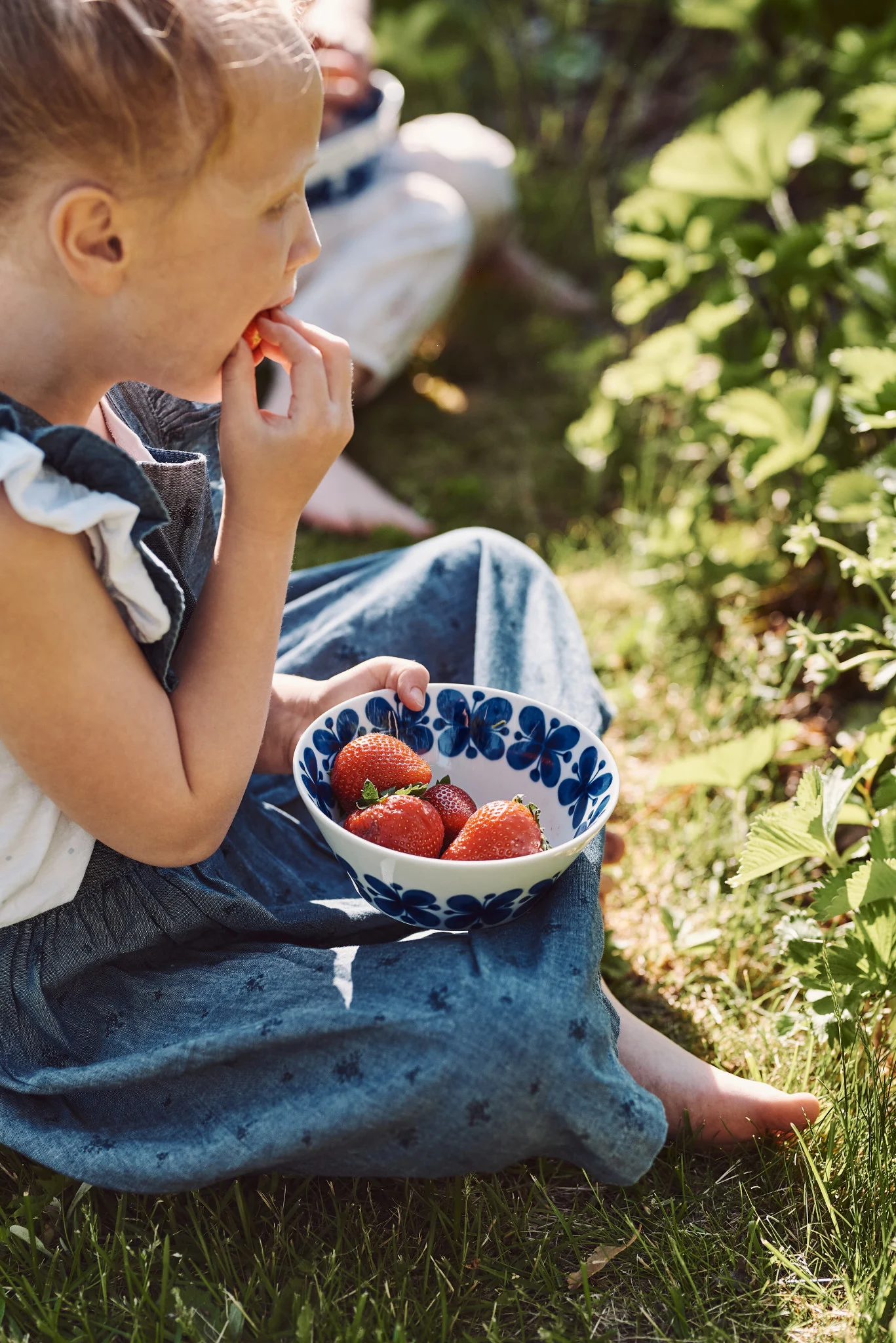Découvrez des recettes estivales simples. Ici, une jeune fille cueille et mange des fraises dans un bol bleu et blanc.