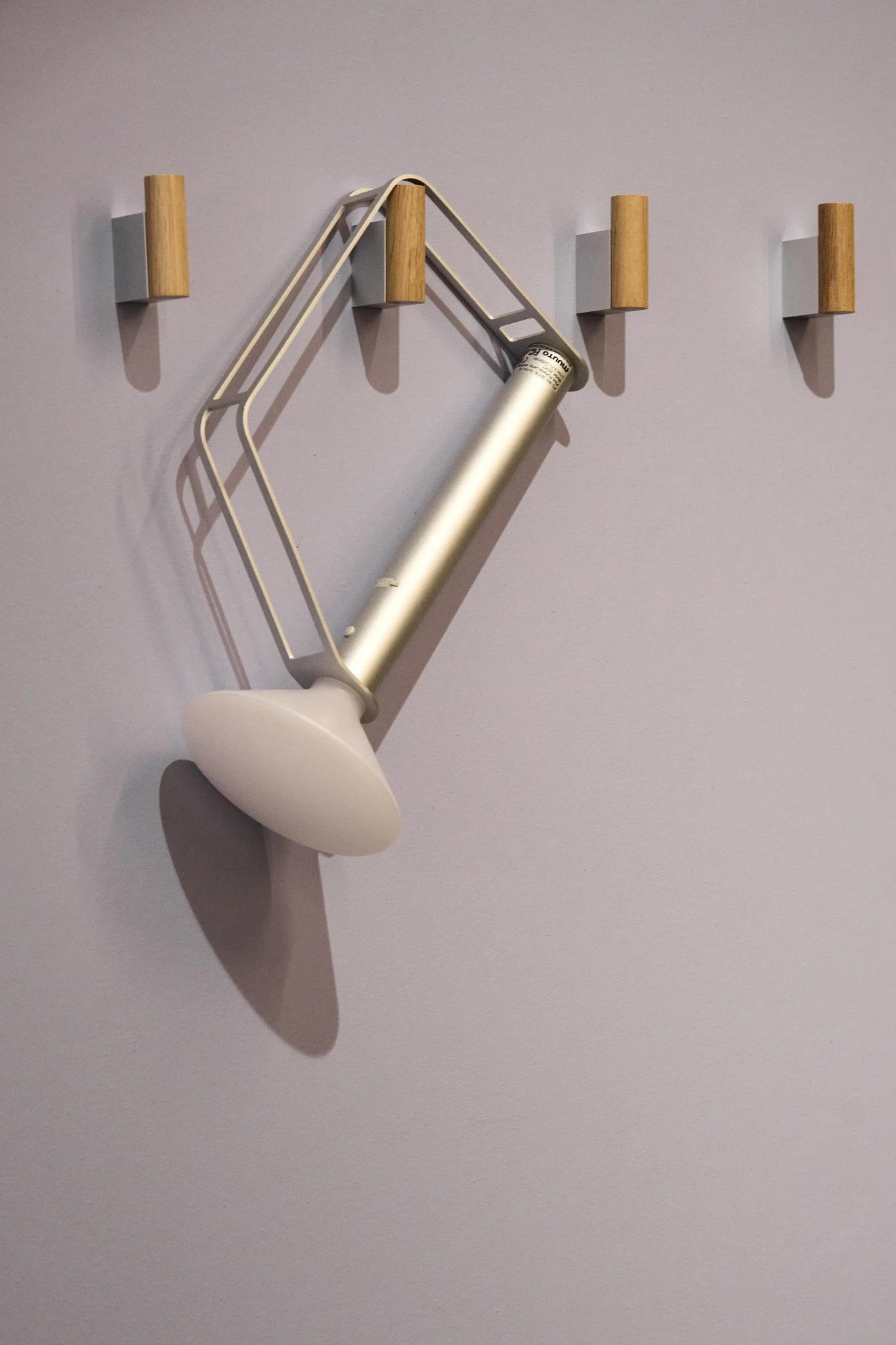 La lampe de table Piton de Muuto, argentée et portable, est suspendue à l'un des quatre crochets fixés au mur.