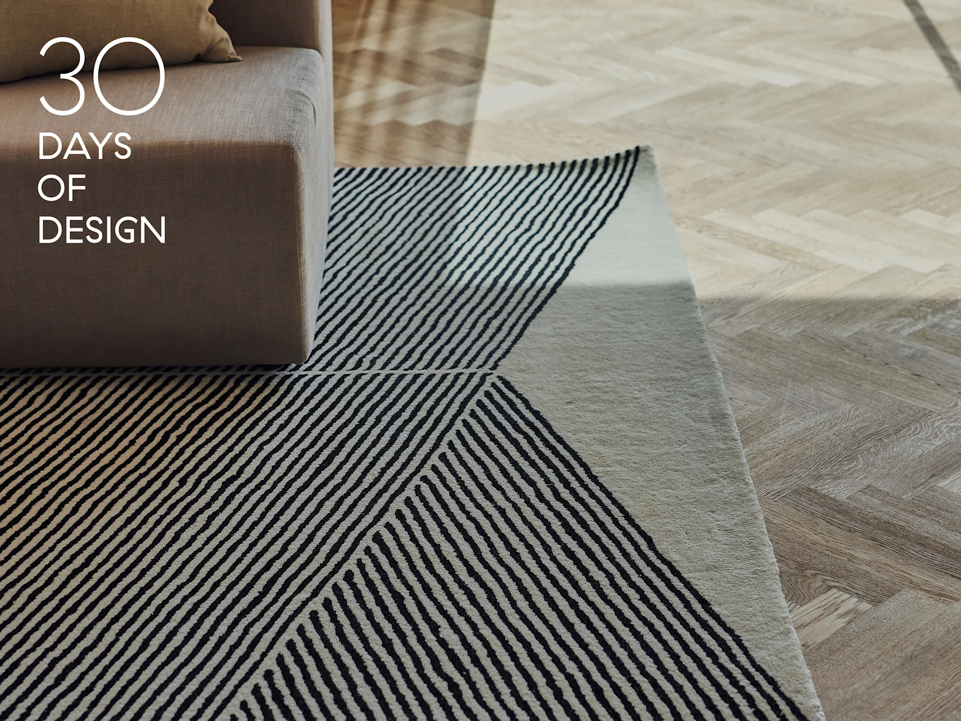 Accoudoir de canapé, tapis à rayures géométriques noires et blanches et parquet en chevrons clair. Texte : 30 DAYS OF DESIGN.