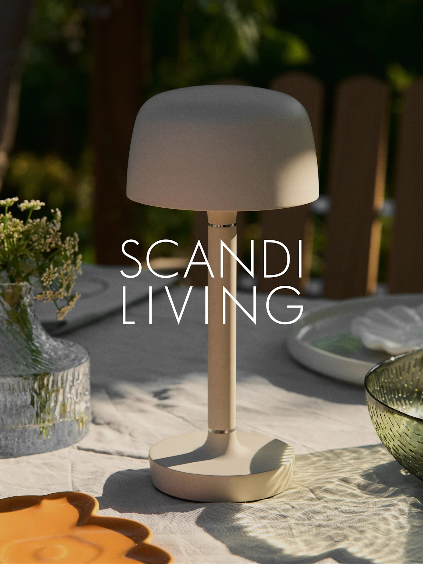 Une lampe de table portable moderne beige sur une table d'extérieur avec un vase de fleurs et de la vaisselle. Texte "SCANDI LIVING".