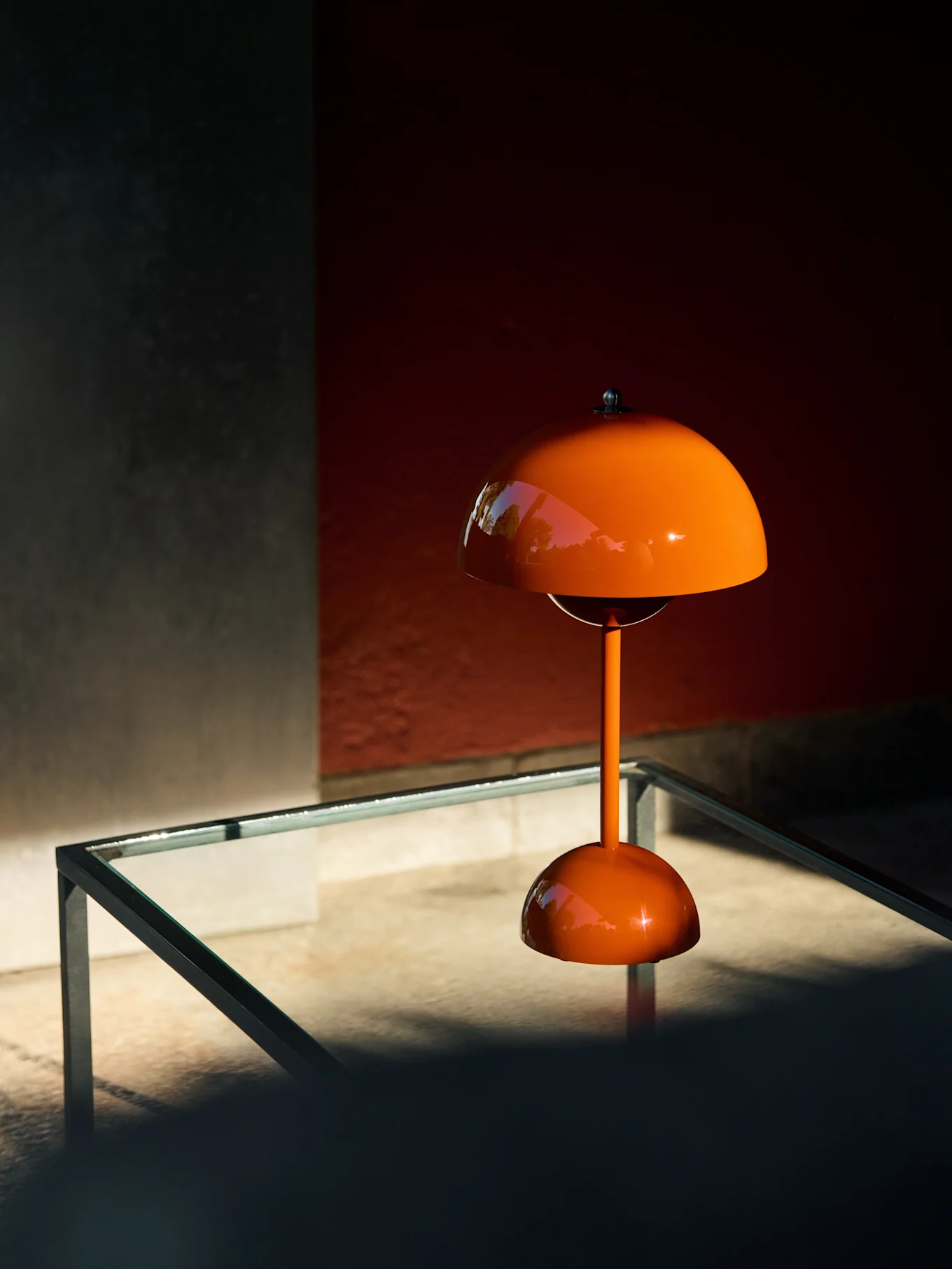Lampe de table orange en forme de champignon sur une table en verre, reflétant la verdure.