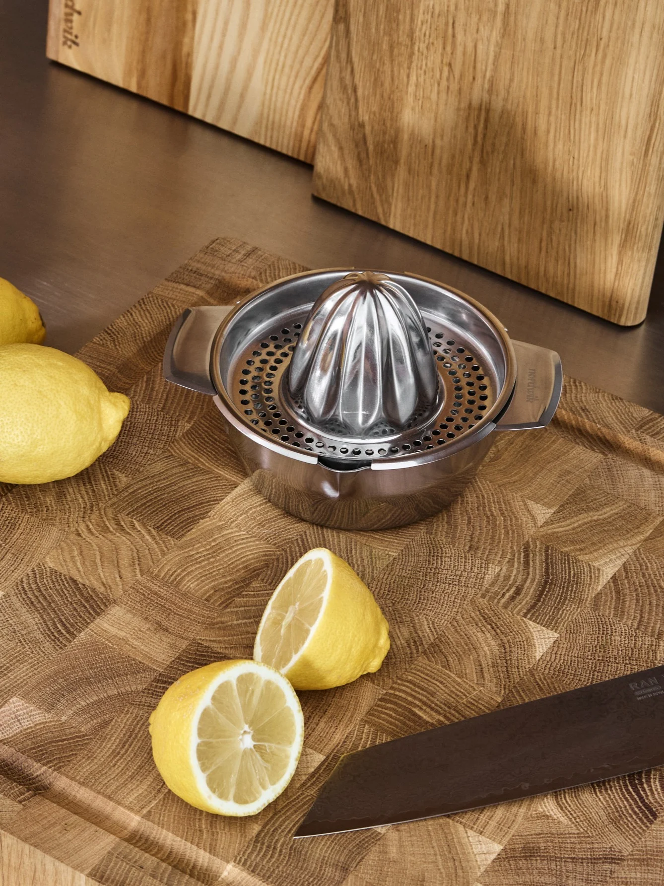 Presse-citron manuel en acier inoxydable, citrons entiers et coupés, et un couteau sur une planche à découper en bois.
