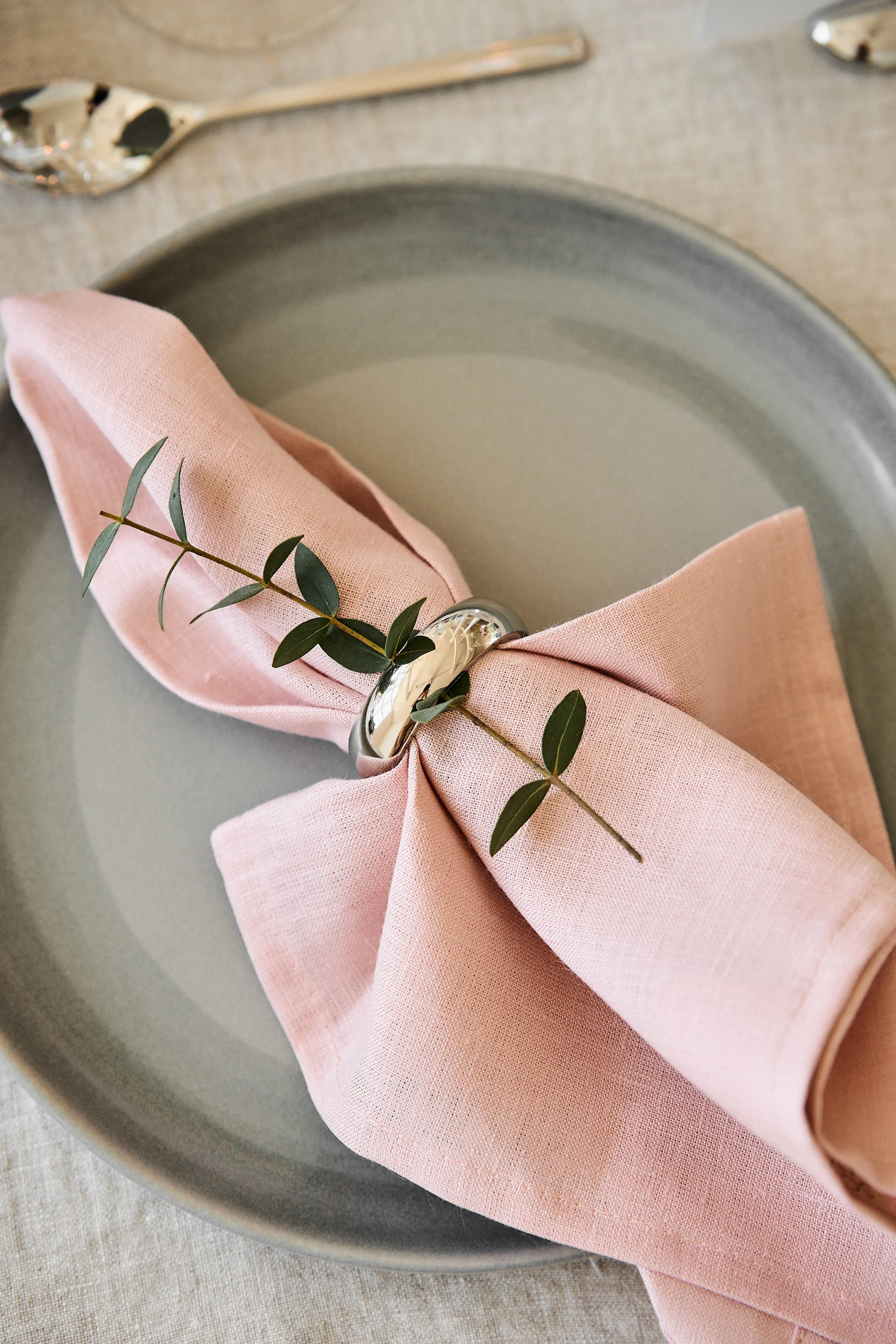 Décorez la table de votre repas romantique à la maison avec des couleurs agréables. Ici, la serviette Clean en Dusty Rose de Scandi Living est posée sur une assiette avec un rond de serviette.