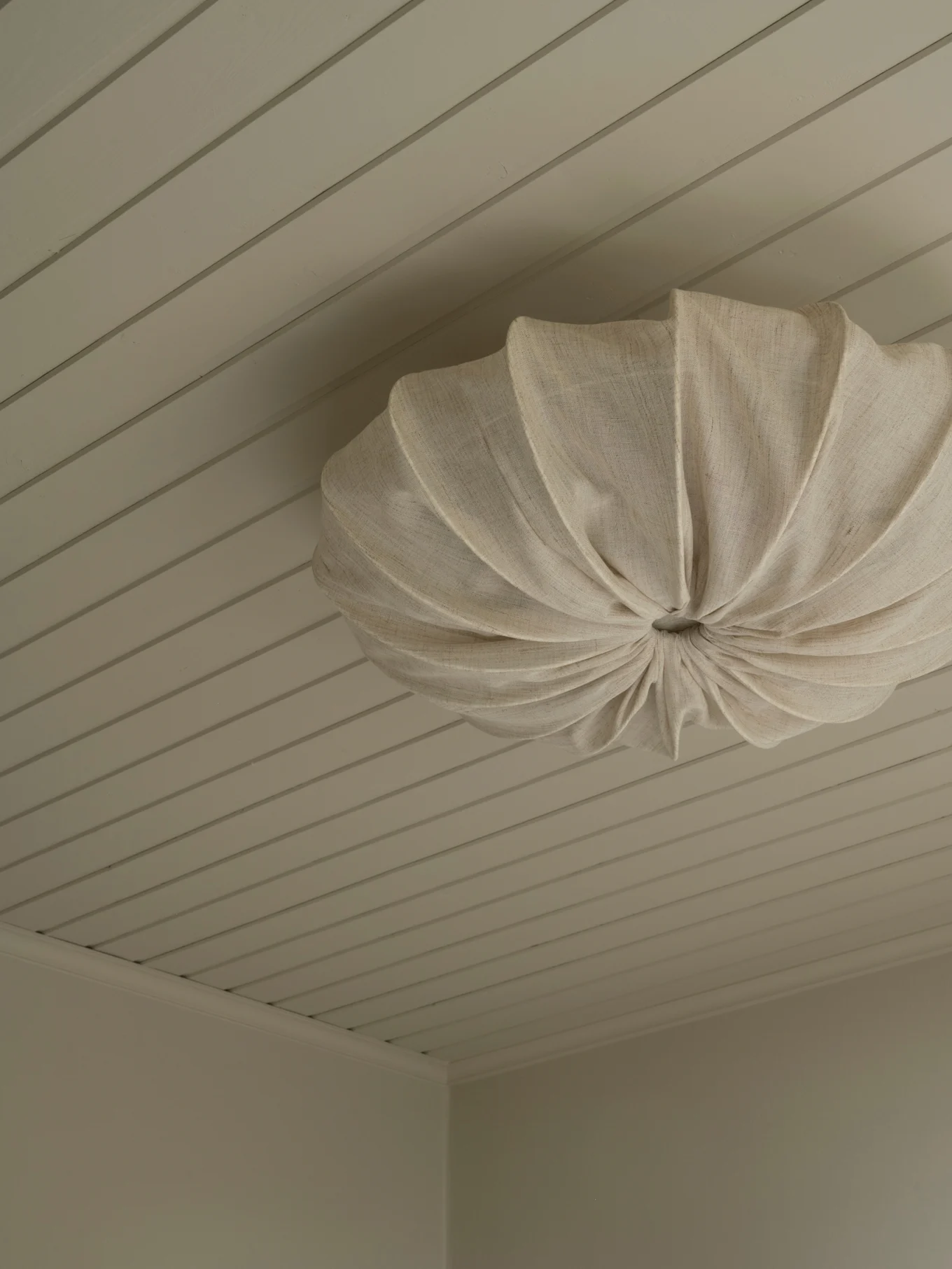 Un plafonnier en tissu plissé crème monté sur un plafond à panneaux clairs.