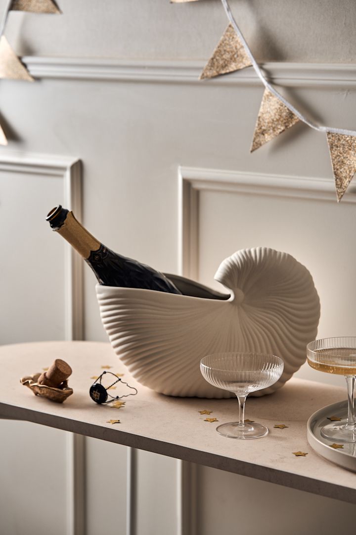 Découvrez comment organiser une fête avec une station de boissons : ici, vous voyez une bouteille de champagne refroidissant dans le vase Shell de Ferm Living, avec des coupes de champagne disposées sur une table en tant que station de boissons en libre-service.
